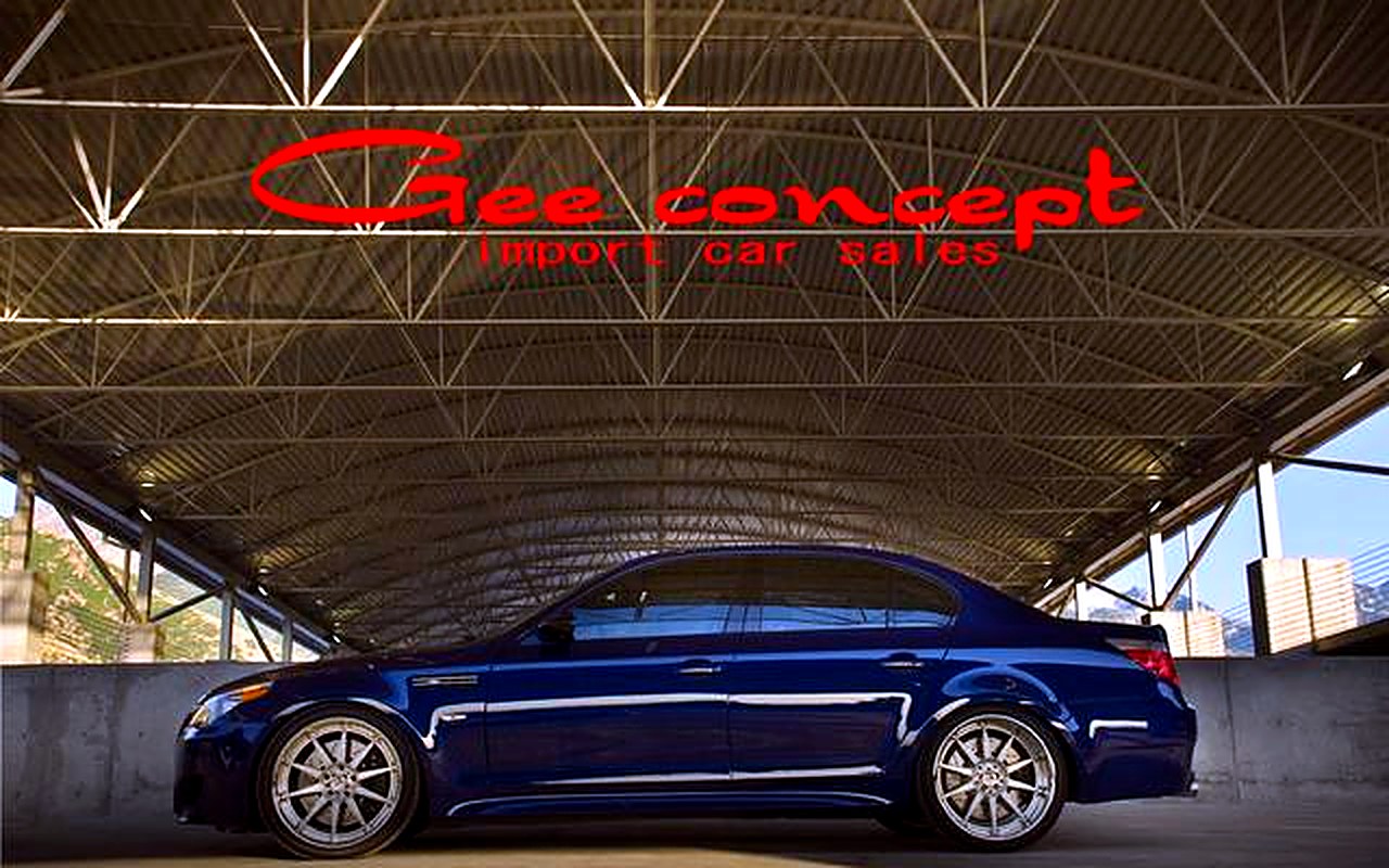 鉄骨大屋根に掲げられた赤いGee conceptロゴ看板と紺のBMWセダン（グーネット店舗ページ掲載・実写真／色調補正済み）